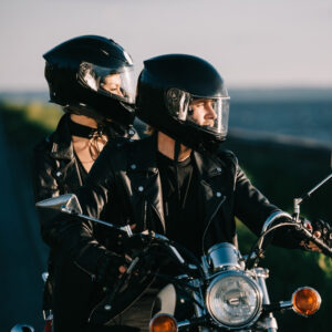 A man and woman sitting on a parked motorcycle and wearing helmets.